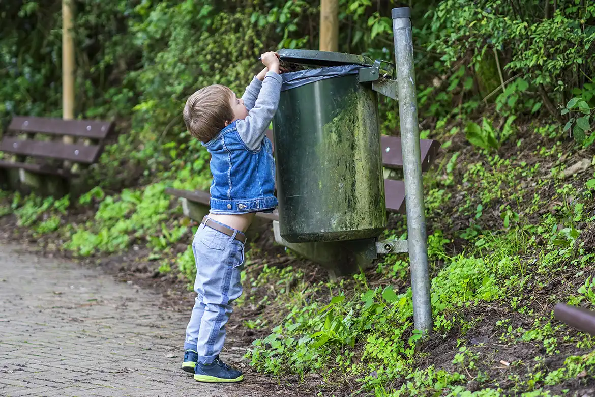 Liten gutt som kaster søppel i en søppeldunk i parken