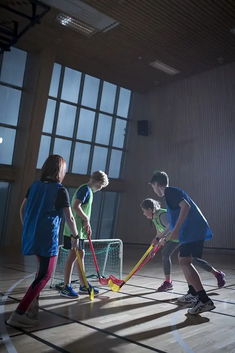 Fire barn som spiller innebandy i en gymsal
