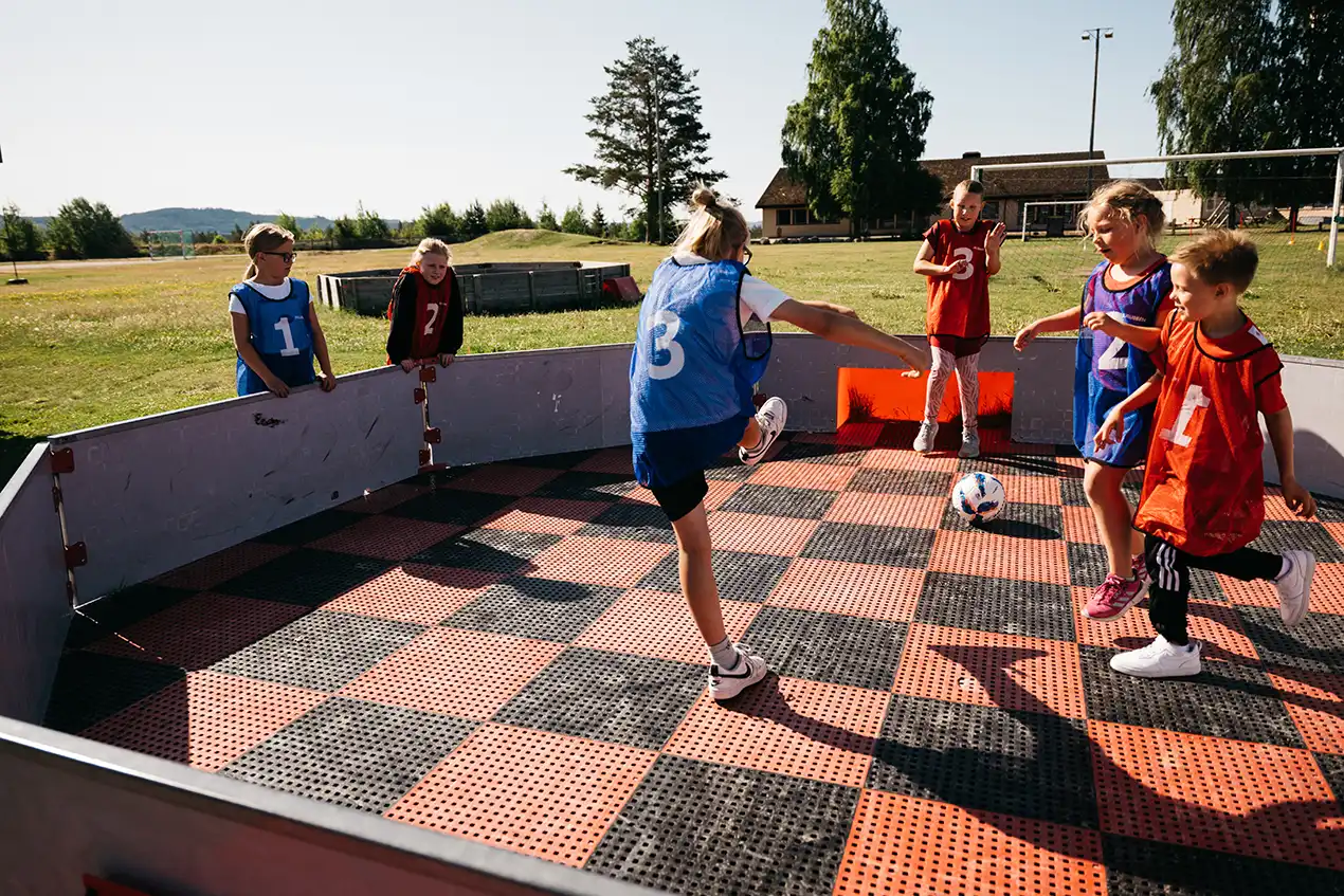 Glade barn som spiller fotball i en ballbinge utendørs