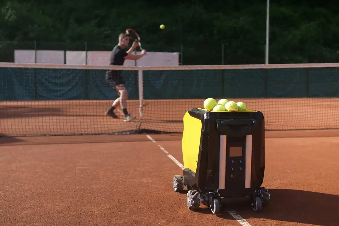 Mann som spiller tennis utendørs alene - han har en ballmaskin som kaster baller til han