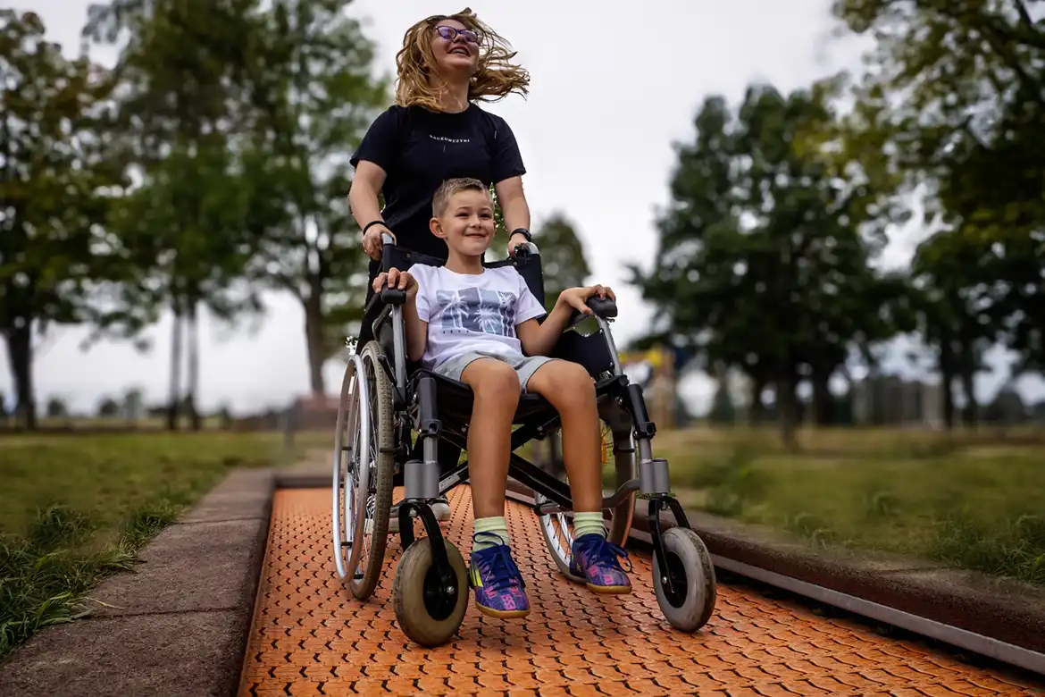 En ung gutt som sitter i rullestol, hopper på bakketrampoline sammen med en venn