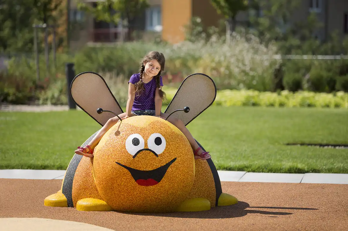 Jente som sitter på toppen av en gummifigur som ser ut som en bie
