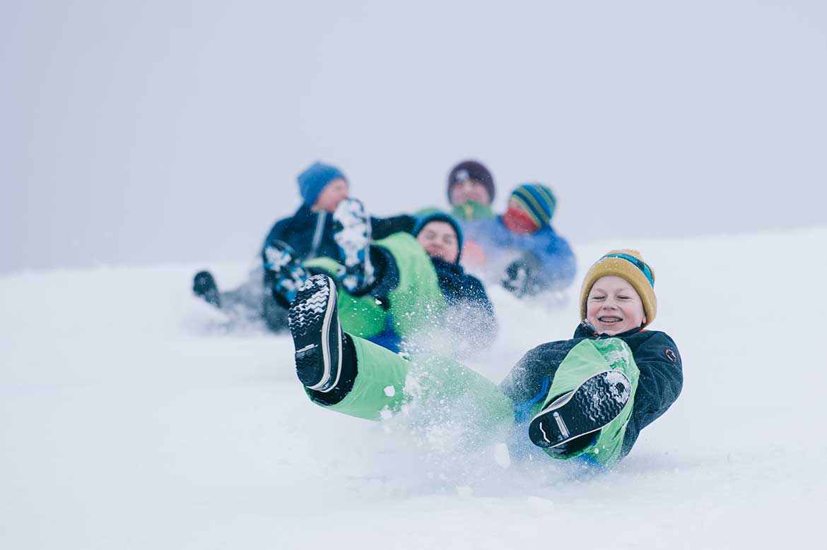 Flere barn på rumpeakebrett nedover en akebakke
