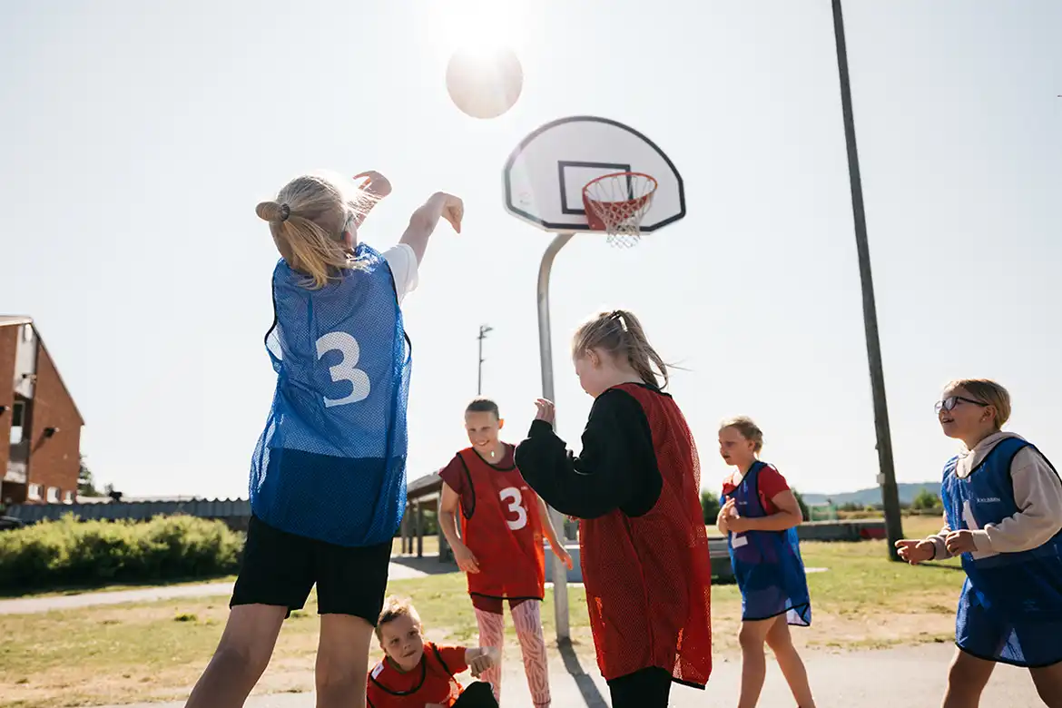 En gjeng glade barn spiller basketball utendørs