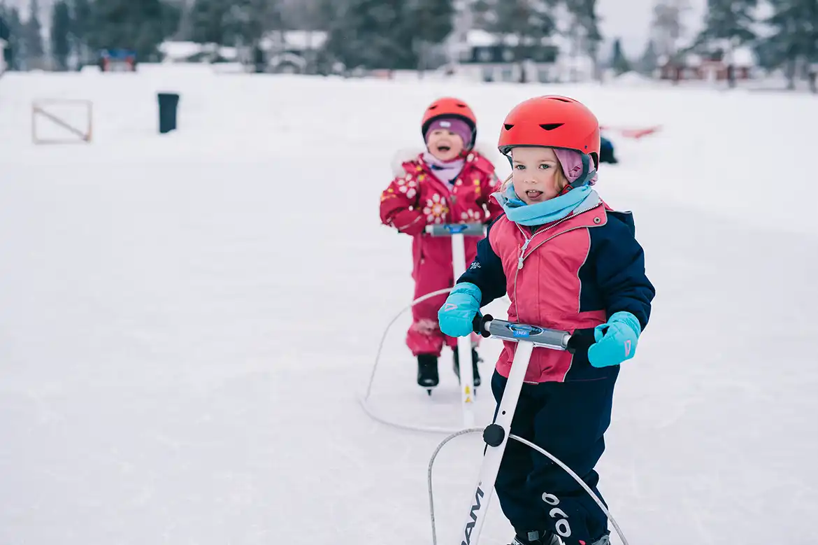 To små blide jenter som går på skøyter med hjelp av skøytestøtte - de har på seg hjelm